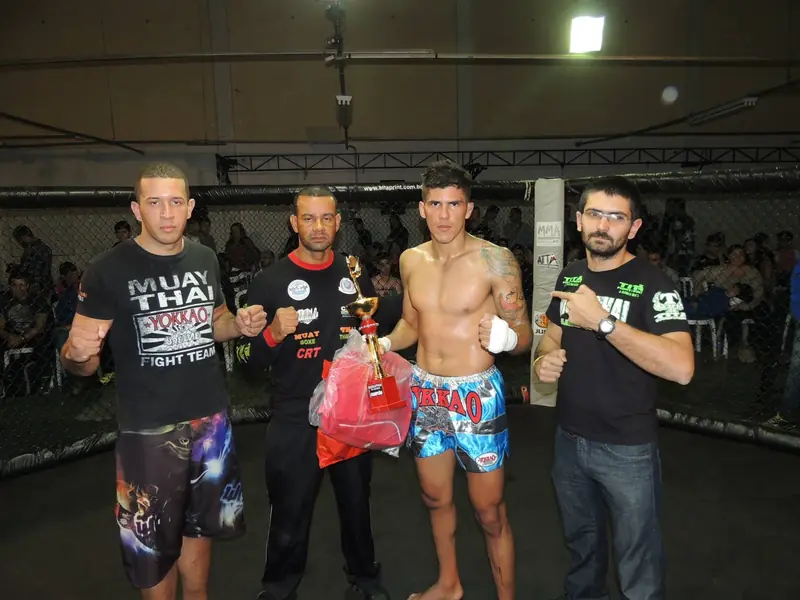Kevem com um troféu de muay thai no cage, com a equipe