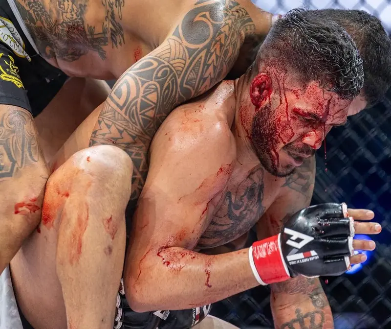 Kevem, com o rosto ensanguentado, agarrado ao adversário no chão do cage